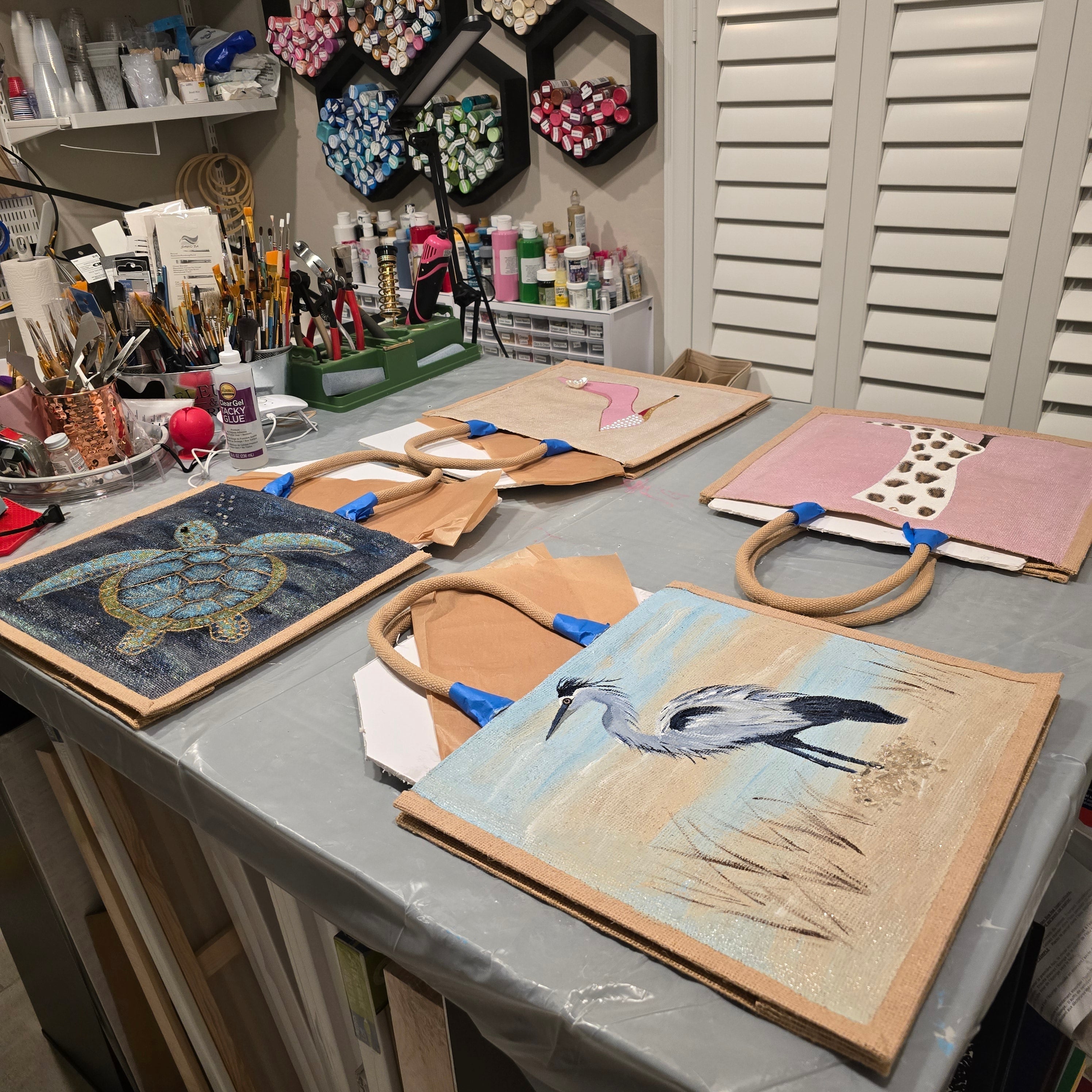 Hand-painted tote bags in progress featuring sea turtle, heron, and shoe designs.
