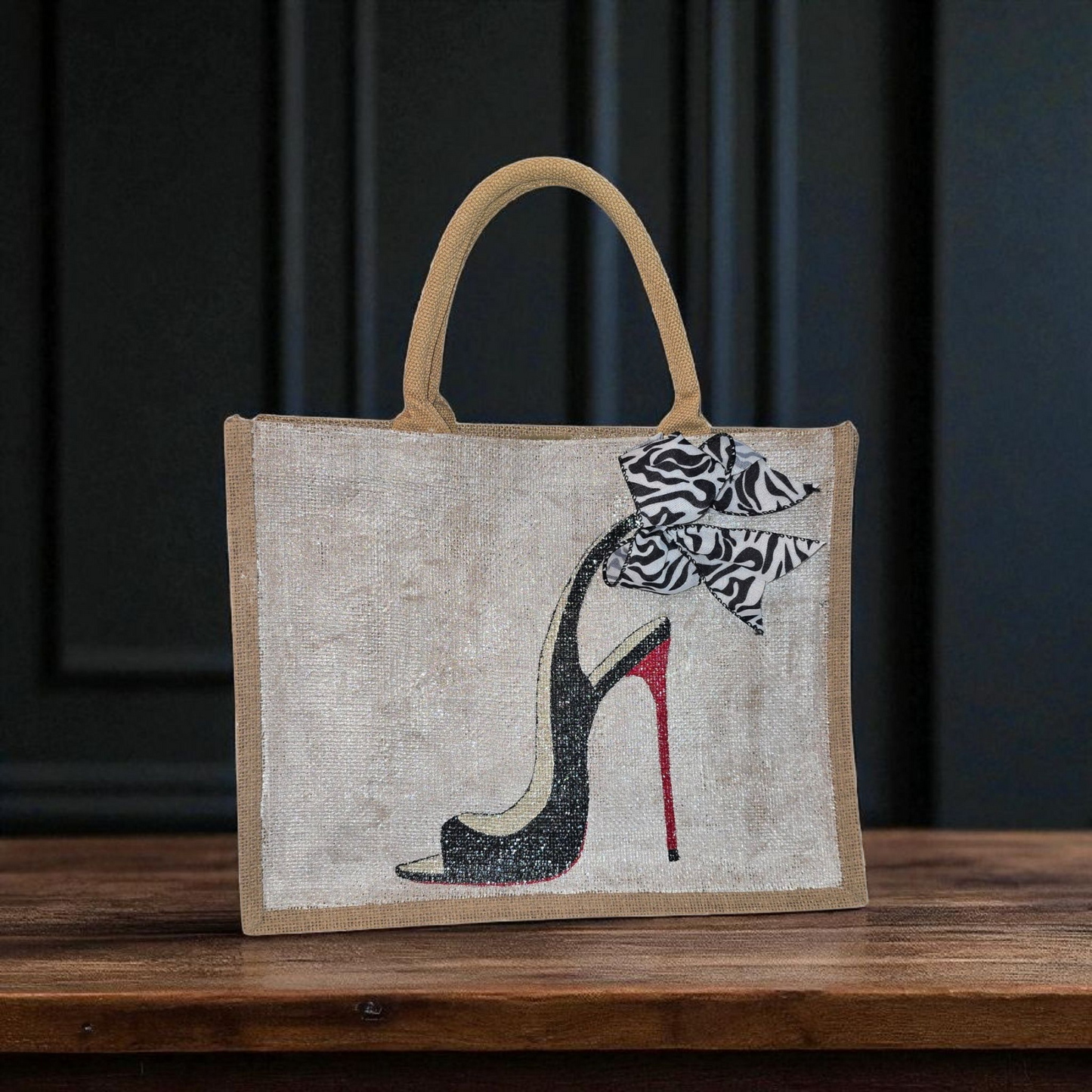 Hand-painted jute tote bag featuring a black stiletto heel with red sole and a zebra-print bow, designed by Dana’s Uncommon Glass