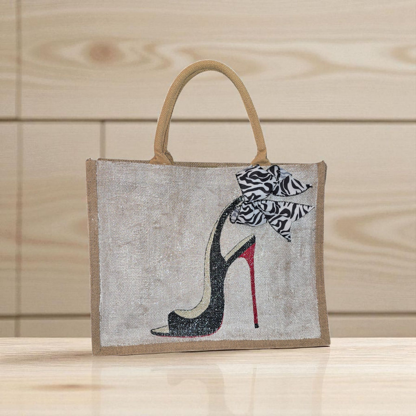 Hand-painted jute tote bag featuring a black stiletto heel with red sole and a zebra-print bow, designed by Dana’s Uncommon Glass