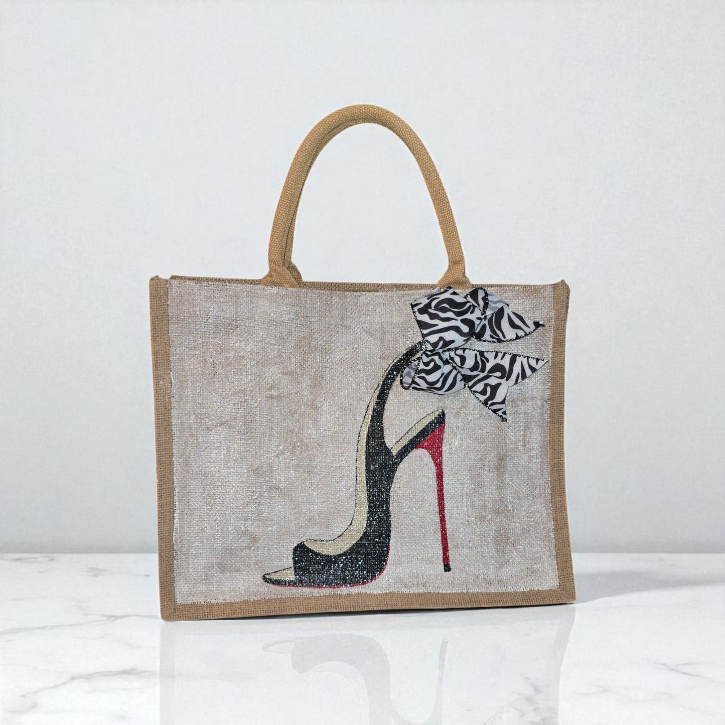 Hand-painted jute tote bag featuring a black stiletto heel with red sole and a zebra-print bow, designed by Dana’s Uncommon Glass