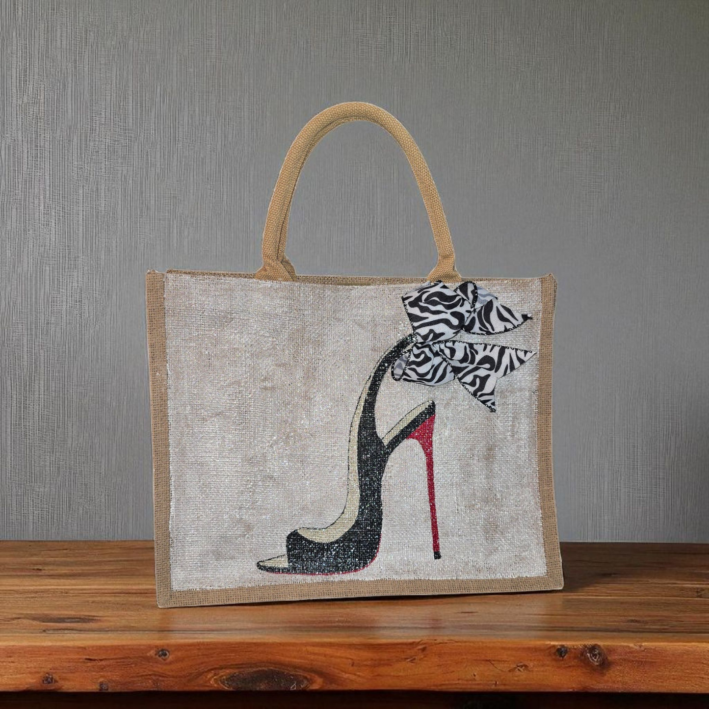 Hand-painted jute tote bag featuring a black stiletto heel with red sole and a zebra-print bow, designed by Dana’s Uncommon Glass