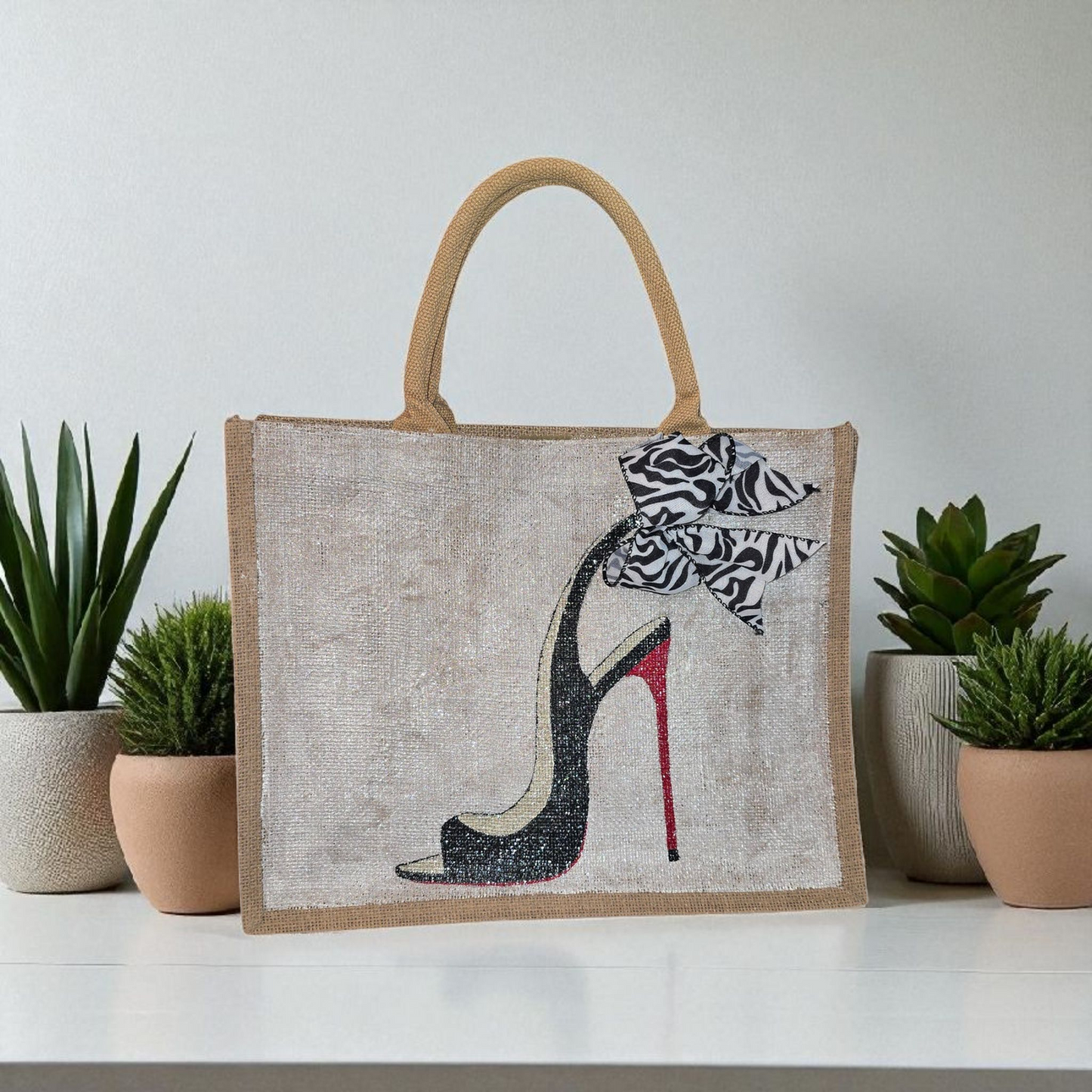 Hand-painted jute tote bag featuring a black stiletto heel with red sole and a zebra-print bow, designed by Dana’s Uncommon Glass
