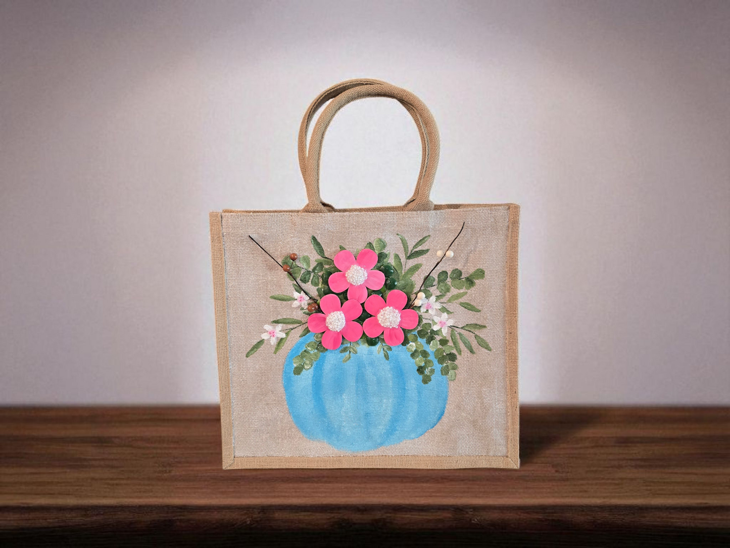 Hand-painted jute tote featuring a blue pumpkin used as a flower pot, filled with pink flowers and greenery; painted on off-white metallic background with beads, leaves, and wooden floral embellishments