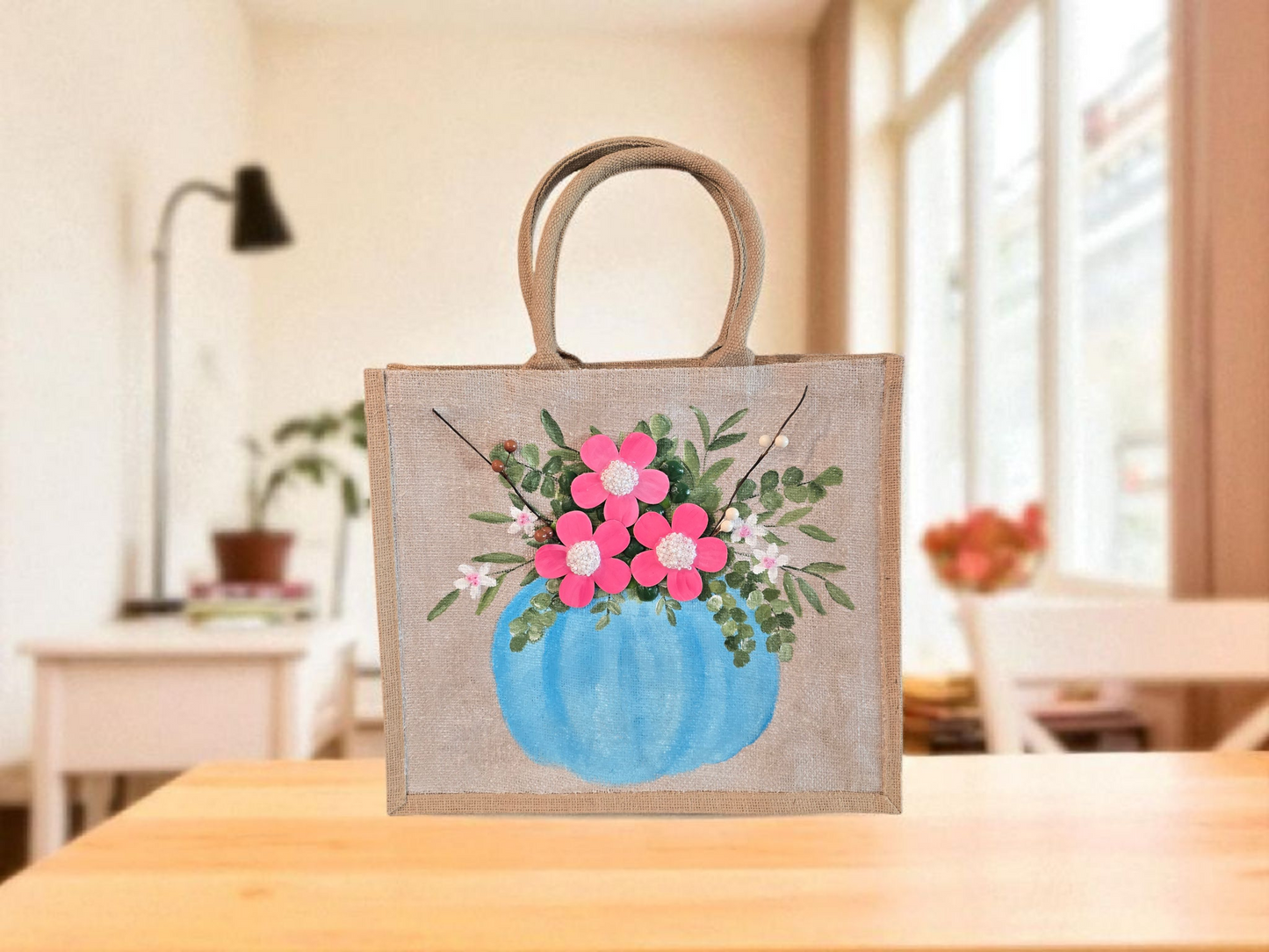 Hand-painted jute tote featuring a blue pumpkin used as a flower pot, filled with pink flowers and greenery; painted on off-white metallic background with beads, leaves, and wooden floral embellishments