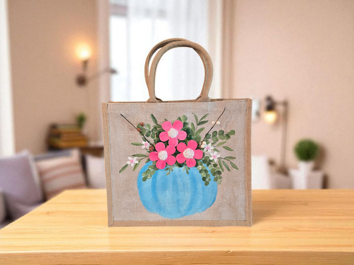 Hand-painted jute tote featuring a blue pumpkin used as a flower pot, filled with pink flowers and greenery; painted on off-white metallic background with beads, leaves, and wooden floral embellishments
