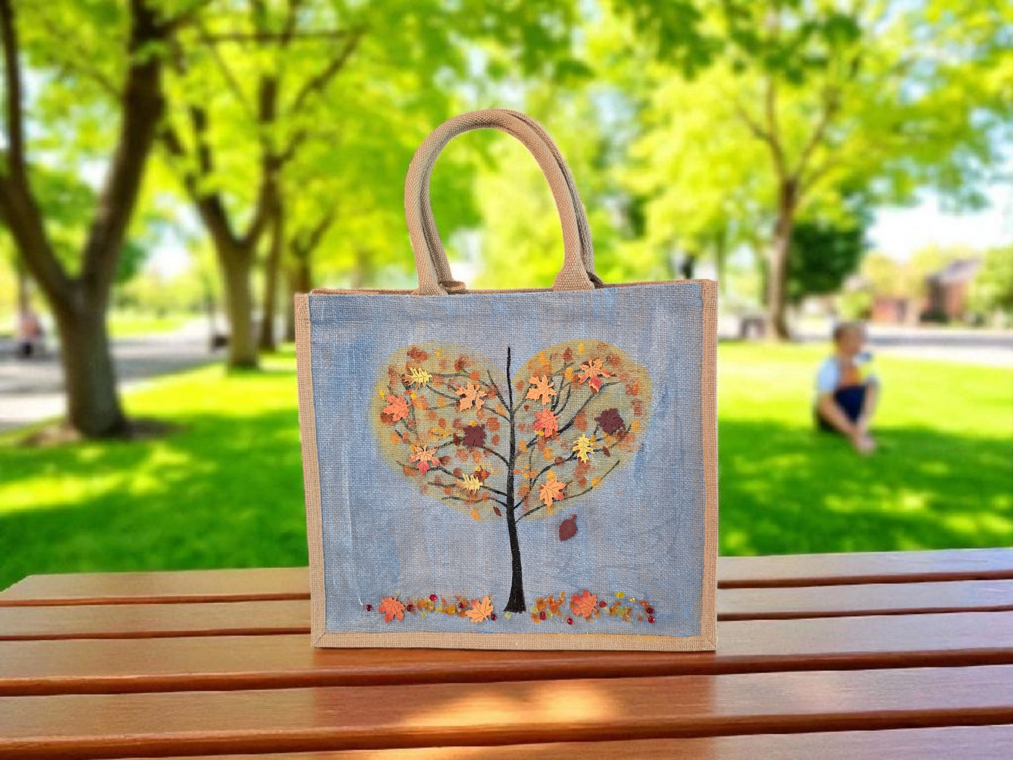 Hand-painted jute tote featuring a heart-shaped fall tree with colorful leaves in red, orange, and gold; painted on a pale blue metallic background with beads and wooden embellishments