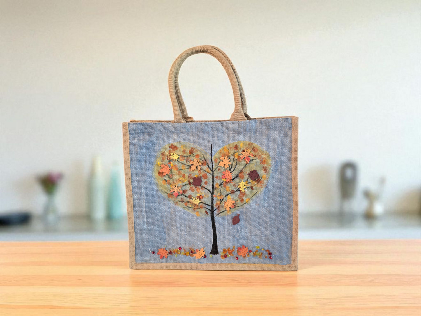 Hand-painted jute tote featuring a heart-shaped fall tree with colorful leaves in red, orange, and gold; painted on a pale blue metallic background with beads and wooden embellishments