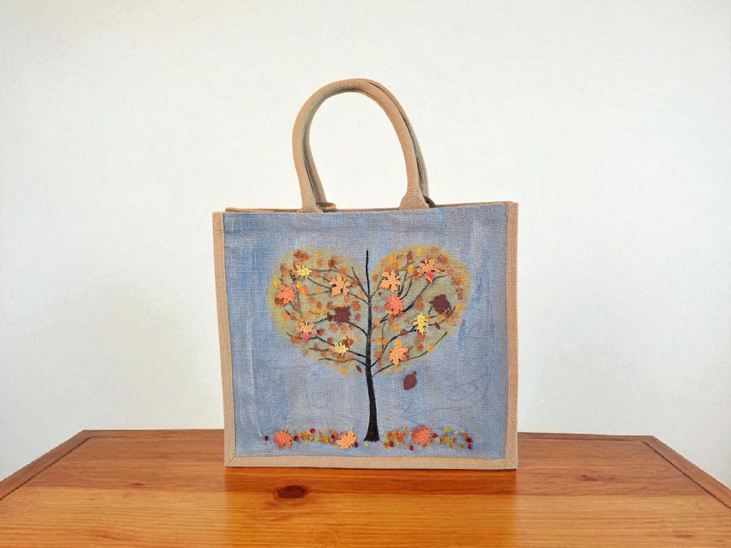 Hand-painted jute tote featuring a heart-shaped fall tree with colorful leaves in red, orange, and gold; painted on a pale blue metallic background with beads and wooden embellishments