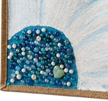 Close up of Hand-painted jute tote bag featuring oversized white floral petals on a bright turquoise blue background with blue, pearl, and crystal bead embellishments at the flower center, finished with natural jute trim and rounded padded handles.