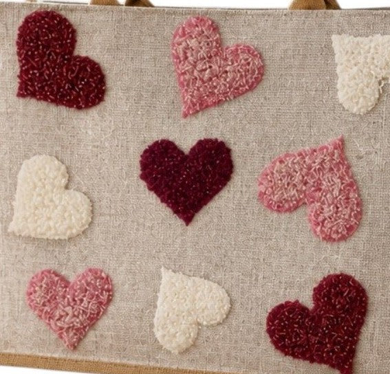 close up of Hand-painted jute shopper bag featuring textured tufted hearts in pink, burgundy, and cream on a natural canvas background with tan handles.