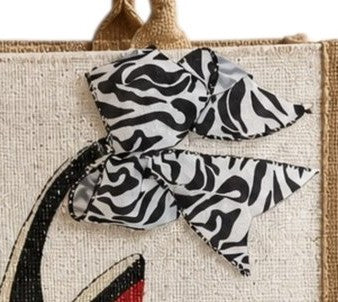 close up of Hand-painted natural jute shopper tote featuring a black stiletto shoe with a bold zebra-print ribbon bow and red sole accents, designed as chic wearable fashion art.