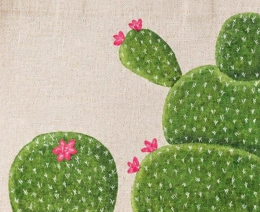 Close up of Hand-painted cactus tote bag featuring whimsical green cactus designs with pink blooms on a natural canvas background, accented with jute trim and rounded padded handles against a neutral background.
