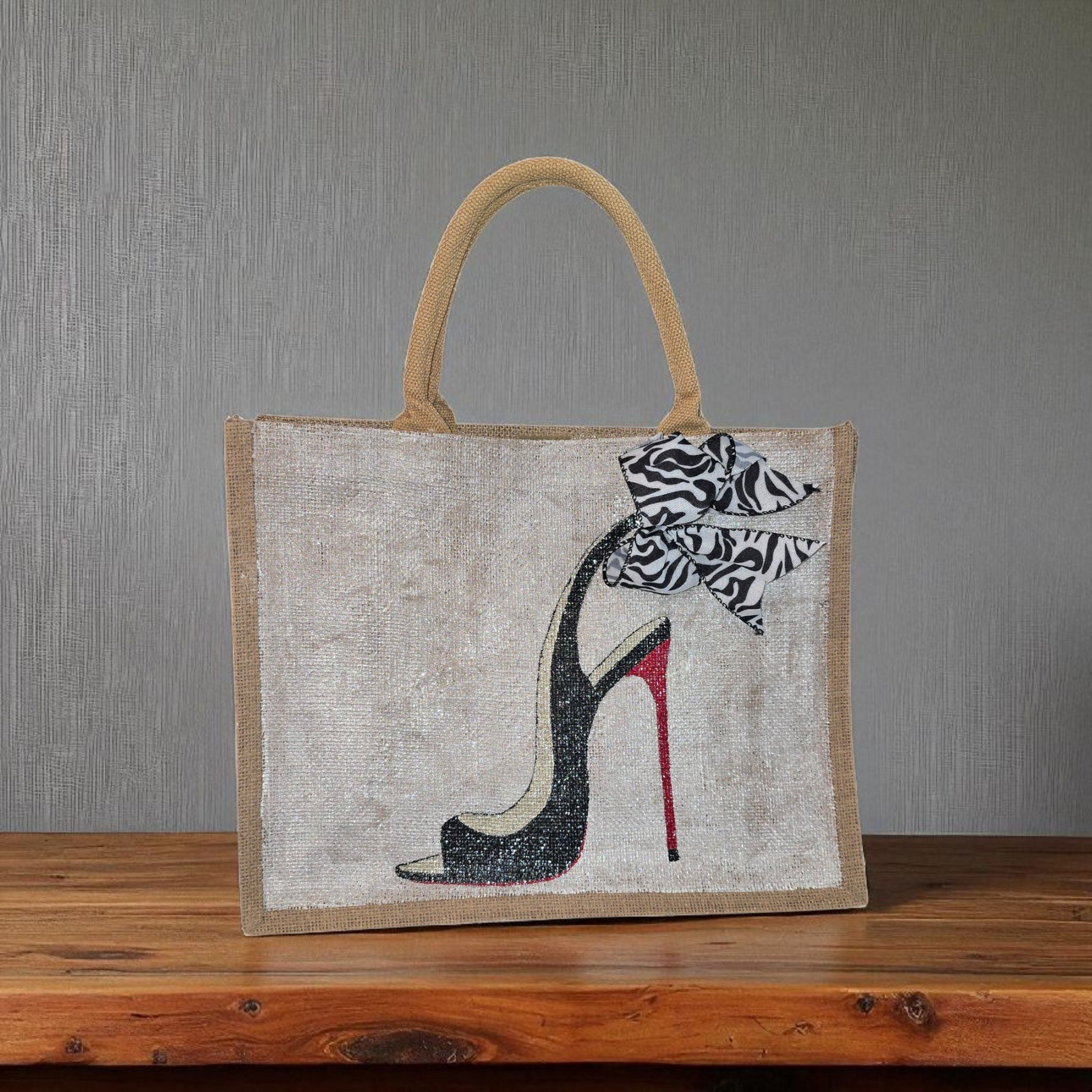 Hand-painted jute tote bag featuring a black stiletto heel with red sole and a zebra-print bow, designed by Dana’s Uncommon Glass