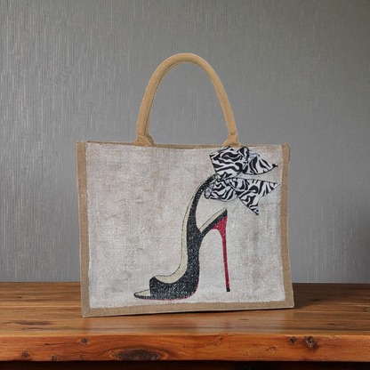 Hand-painted jute tote bag featuring a black stiletto heel with red sole and a zebra-print bow, designed by Dana’s Uncommon Glass