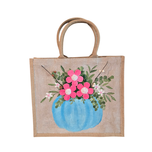 Hand-painted jute tote featuring a blue pumpkin used as a flower pot, filled with pink flowers and greenery; painted on off-white metallic background with beads, leaves, and wooden floral embellishments