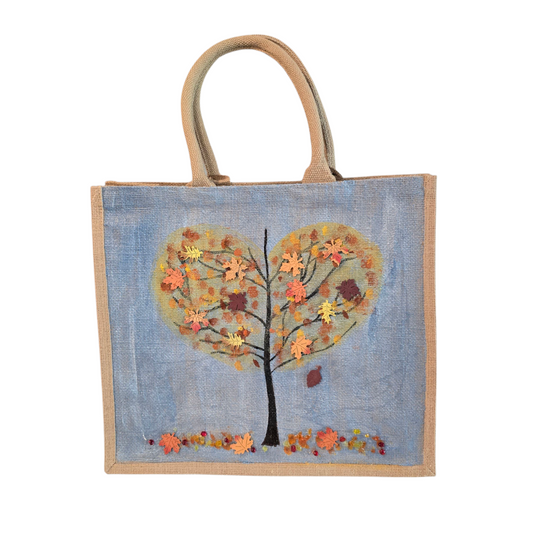 Hand-painted jute tote  featuring a heart-shaped fall tree with colorful leaves in red, orange, and gold; painted on a pale blue metallic background with beads and wooden embellishments 
