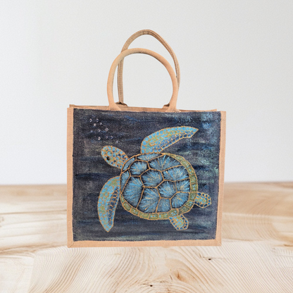 sea turtle hand-painted on burlap jute tote bag in blues, greens and golds on a navy metallic background.