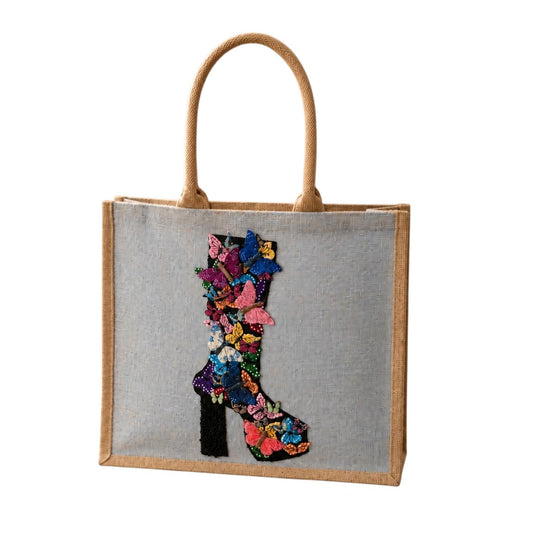 Hand-painted butterfly boot tote bag on soft blue jute canvas featuring a colorful floral and butterfly western boot design, photographed in a neutral boutique-inspired setting with modern styling accents.