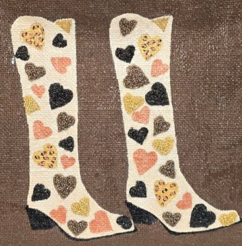close up of Hand-painted western-inspired jute tote bag featuring white cowboy boots decorated with heart designs in black, gold, blush pink, and leopard print accents. Neutral tote bag with a rich brown background and romantic rustic style details.