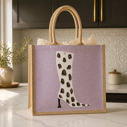 Hand-painted pink jute tote bag featuring a white cow-print western boot design with black and brown spotted detailing, inspired by modern western fashion and wearable art styling.