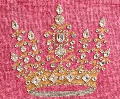 close up of Hand-painted pink jute tote bag featuring an embellished gold crown design with sparkling rhinestones and jewel accents, finished with natural burlap handles and sides.