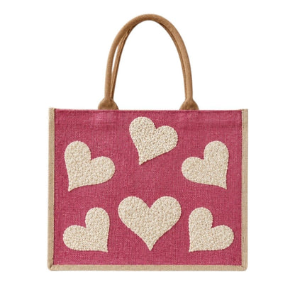 Hand-painted pink jute shopper bag featuring five textured cream hearts on a bright pink background with natural tan handles and trim.