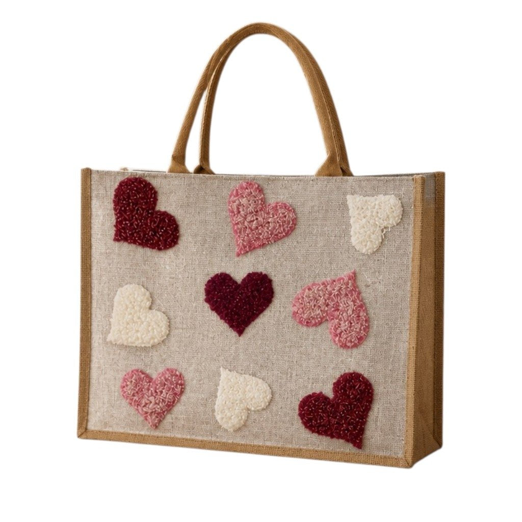 Hand-painted jute shopper bag featuring textured tufted hearts in pink, burgundy, and cream on a natural canvas background with tan handles.