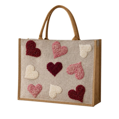 Hand-painted jute shopper bag featuring textured tufted hearts in pink, burgundy, and cream on a natural canvas background with tan handles.