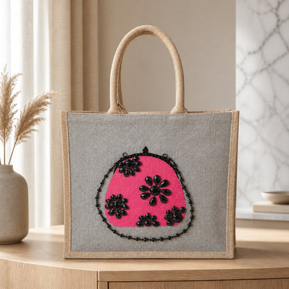 Hand-painted gray jute tote bag featuring a vibrant pink embellished purse design with black jeweled floral accents and sparkling bead details.