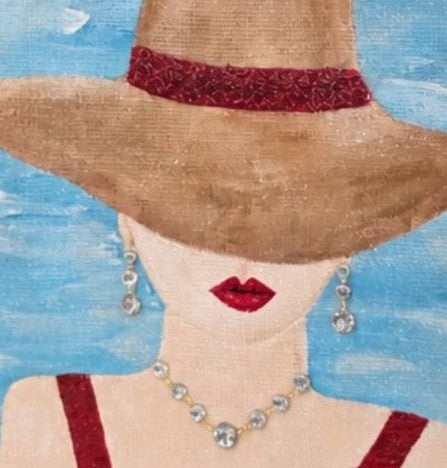 close up of Hand-painted beach lady jute tote bag with wide sun hat, red swimsuit straps, blue sky background, jeweled necklace accents, and natural woven handles.
