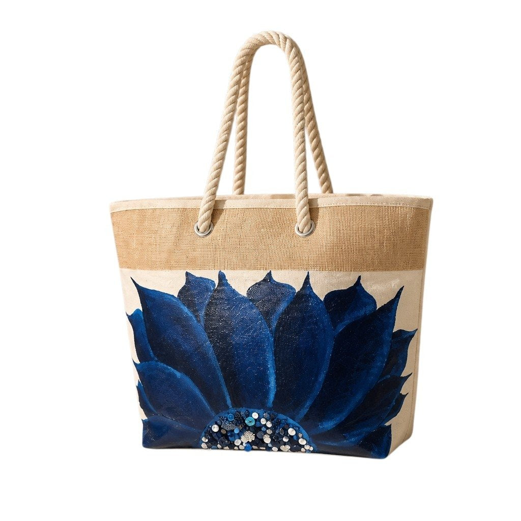 Hand-painted rope handle beach tote featuring a bold navy blue floral design with sparkling jeweled embellishments at the flower center, accented with natural jute trim and oversized cream rope handles against a neutral background.