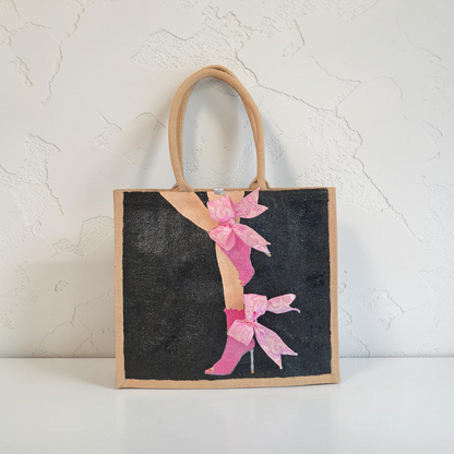 Hand-painted tote bag featuring a pink high heel with bows on a black background with dimensional ribbon accents