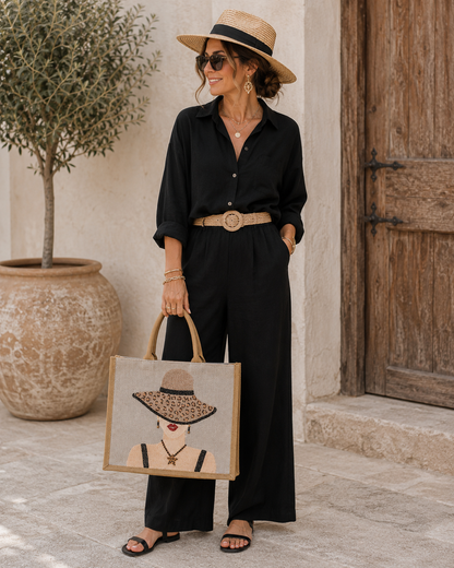 woman holding Hand-painted neutral jute tote bag featuring a stylish woman in a leopard-print sun hat with black straps, red lips, statement earrings, and natural woven handles.
