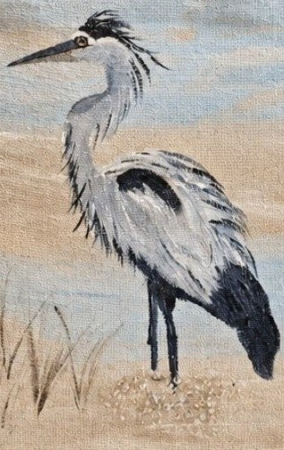 Close up of Hand-painted coastal heron tote bag on natural jute canvas featuring a graceful gray and white heron standing in marsh grass against a soft blue and sandy background.