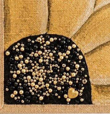 close up of Hand-painted sunflower tote bag featuring soft gold petals on a black background with pearl and gold jeweled embellishments at the flower center, accented with natural jute trim and rounded padded handles against a neutral background.