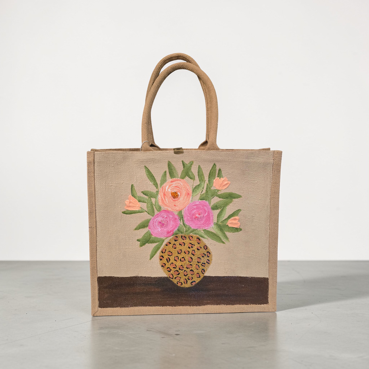 Hand-painted jute tote bag featuring pink and peach flowers arranged in a leopard print vase on a natural canvas background