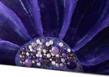 close up of Hand-painted rope handle beach tote featuring a bold purple floral design with jeweled embellishments at the flower center, accented with natural jute trim and oversized cream rope handles against a neutral background.