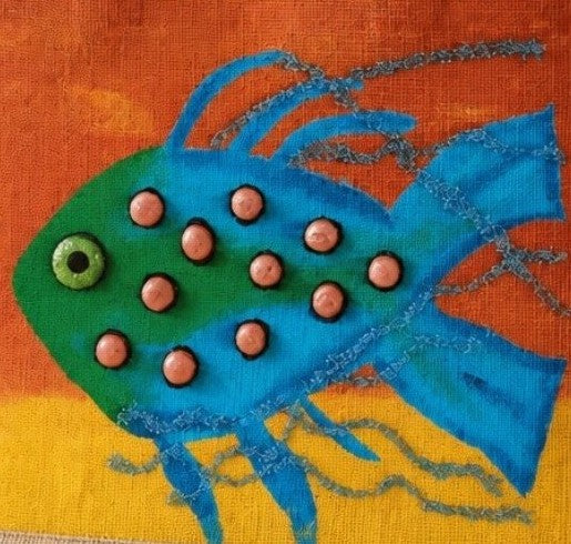 close up of Hand-painted jute tote bag featuring a whimsical blue and green fish with dimensional coral-colored accents on a vibrant orange and yellow background. Coastal-inspired artisan beach tote with rope handles and colorful tropical ocean design.