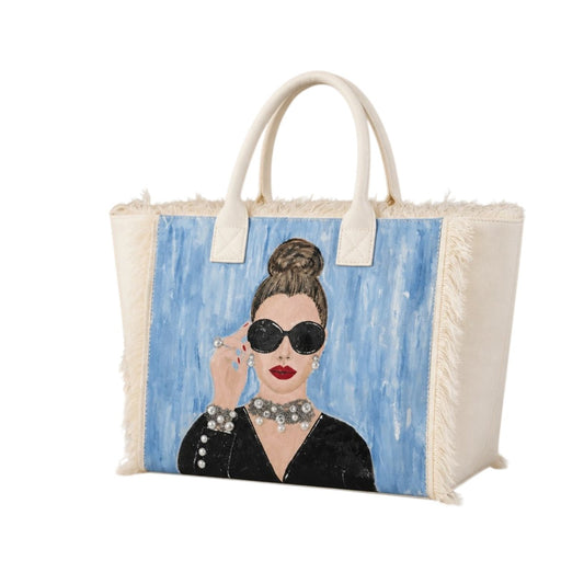 Hand-painted fringed tote bag featuring a glamorous woman with oversized black sunglasses, red lipstick, pearl jewelry, and an elegant updo against a soft blue background on a cream canvas tote.