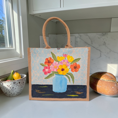 Hand-painted jute tote bag featuring colorful flowers in a blue vase against a light patterned background