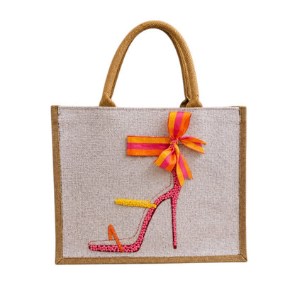 Hand-painted jute tote bag featuring a colorful pink, orange, and yellow embellished stiletto sandal with a striped bow detail and natural woven handles.