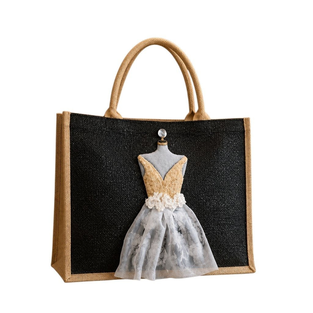 Hand-painted black jute tote bag featuring a dimensional embellished dress design in gold, ivory, and sheer floral fabric against a black background. Elegant bridal-inspired statement tote with textured mixed-media details, natural jute trim, double handles, and magnetic snap closure. Perfect for weddings, bridal showers, fashion lovers, and unique handmade gift giving.