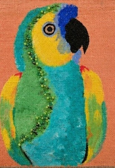 close up of Hand-painted tropical parrot tote bag on natural jute canvas featuring a colorful blue, green, and yellow parrot against a coral-orange background, finished with sturdy double handles and a structured rectangular shape.