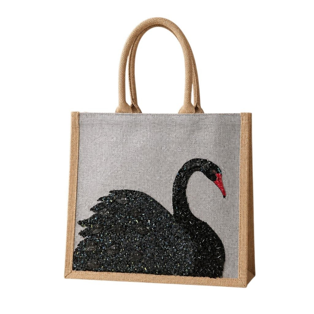 Hand-painted gray jute tote bag featuring an embellished black swan design with textured shimmer details and a red beak. The structured tote has natural woven handles and a sophisticated neutral color palette inspired by elegant, artisan-style fashion accessories.
