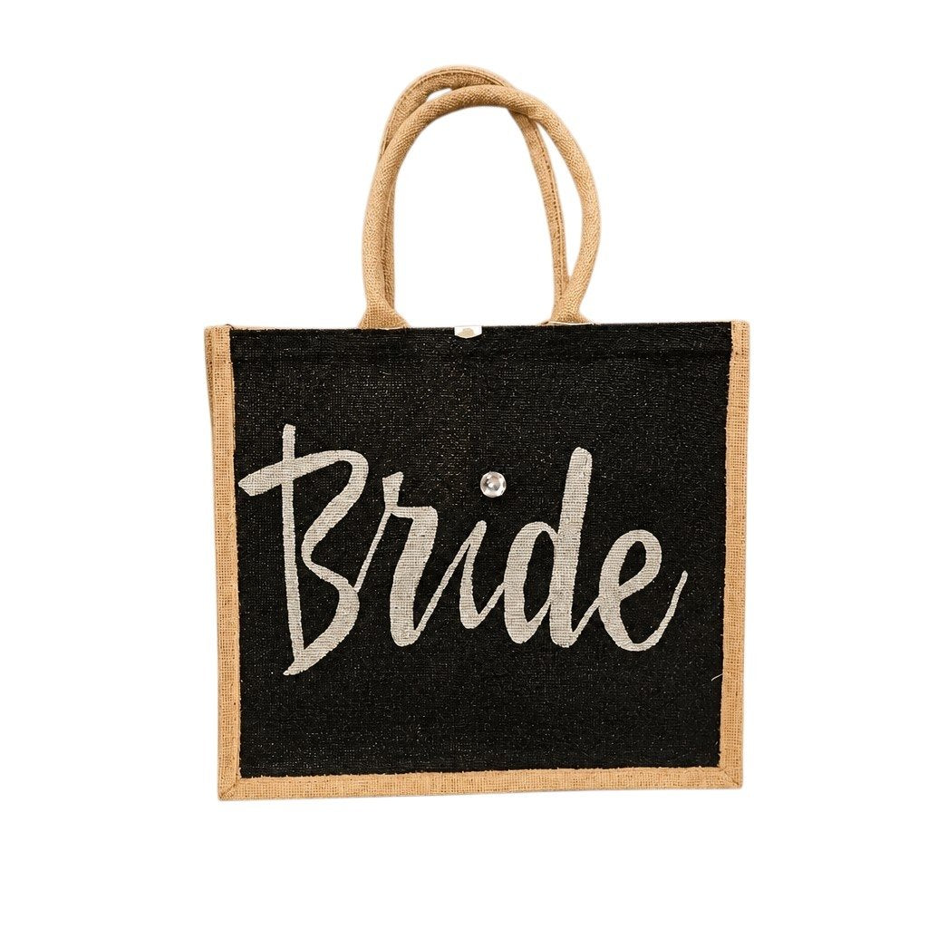 Hand-painted black jute tote bag featuring the word “Bride” in bold white script with a rhinestone accent, designed for weddings, bridal celebrations, and stylish bride-to-be gifts.