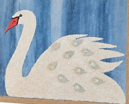 Close up of Hand-painted jute tote bag featuring a white swan with jeweled feather accents on a textured blue background, finished with natural braided handles and coastal-inspired style.