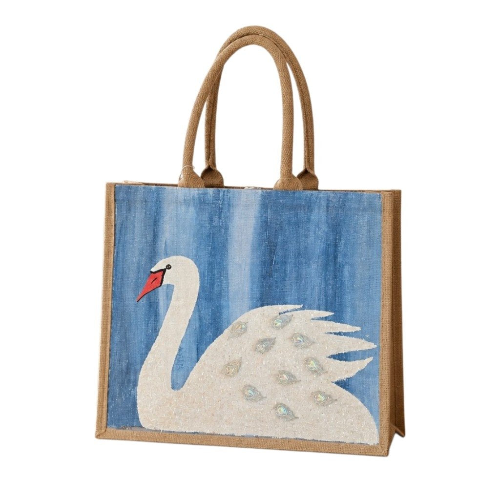 Hand-painted jute tote bag featuring a white swan with jeweled feather accents on a textured blue background, finished with natural braided handles and coastal-inspired style.