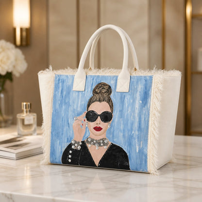 Hand-painted fringed tote bag featuring a glamorous woman with oversized black sunglasses, red lipstick, pearl jewelry, and an elegant updo against a soft blue background on a cream canvas tote.