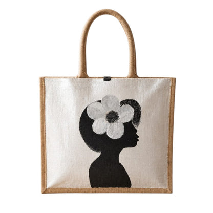Hand-painted jute tote bag featuring a minimalist black silhouette of a woman in profile with a bold white flower in her hair on a pearl white background. This chic neutral tote includes natural jute handles, a magnetic closure, and modern wearable art styling.