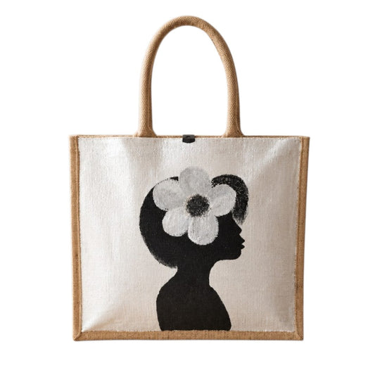 Hand-painted jute tote bag featuring a minimalist black silhouette of a woman in profile with a bold white flower in her hair on a pearl white background. This chic neutral tote includes natural jute handles, a magnetic closure, and modern wearable art styling.